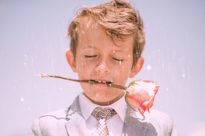 Boy in a suit holding a rose in his mouth
