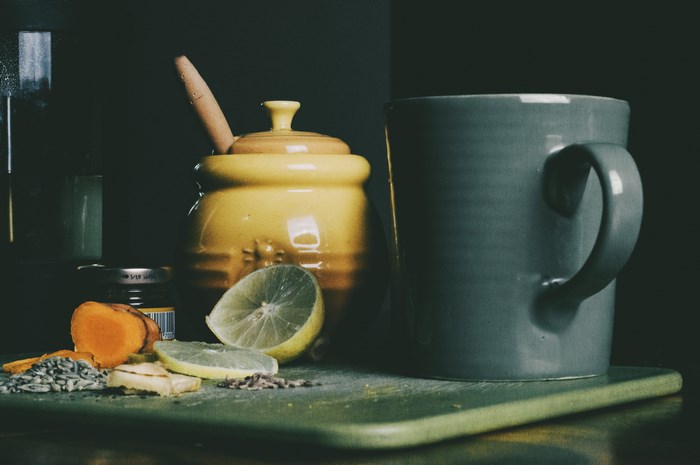 Honey pot, mug, lemon, ginger, and seeds on a chopping board