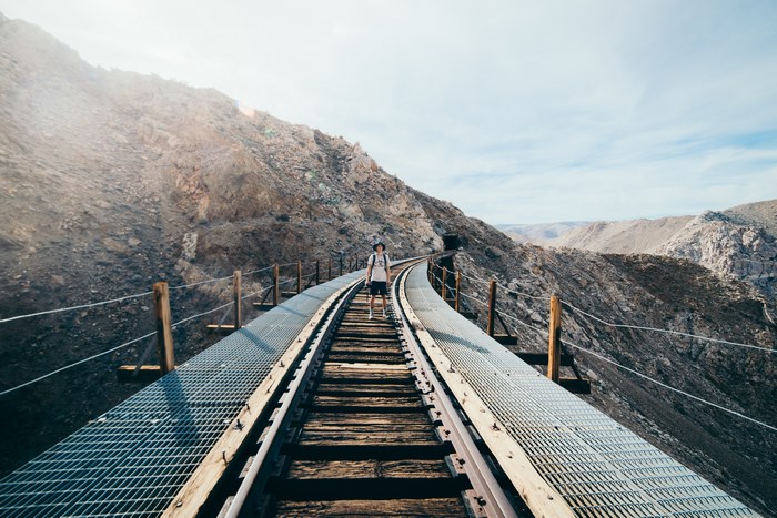 Person standing on a railroad bridge in a mountainous landscape
