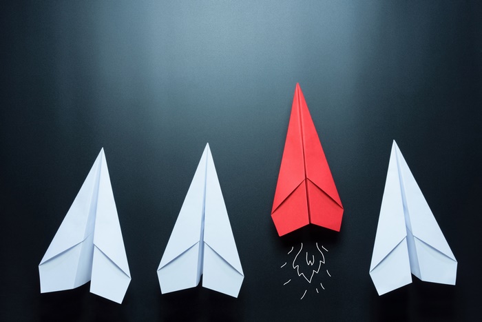 Red paper plane leading white paper planes