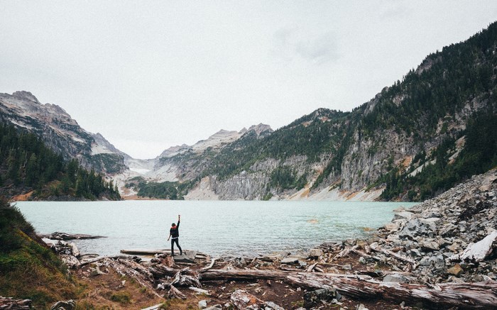 Person standing by a glacier lake with mountains