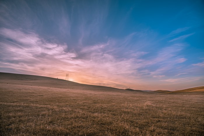 Rural landscape with rolling hills and power lines at sunset