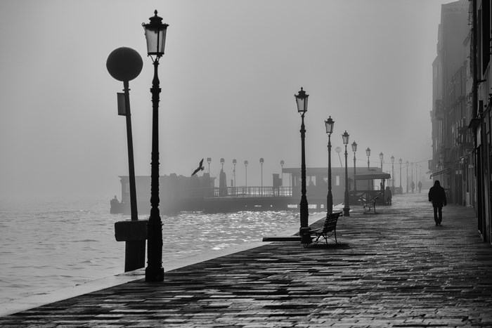 Misty pier with lampposts and a lone pedestrian