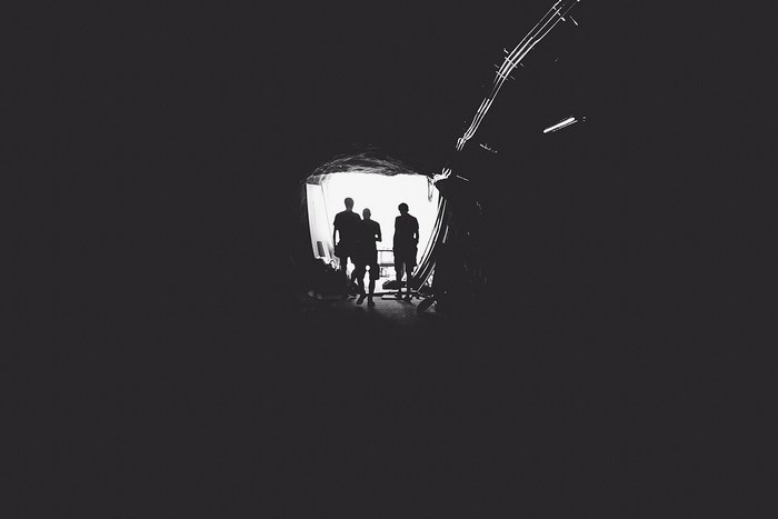 Silhouettes of people in a dark tunnel with light ahead