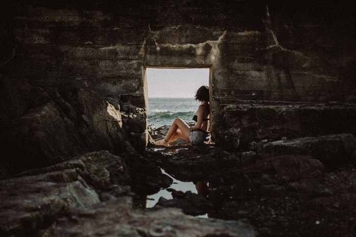 Woman sitting in a stone cave looking at the ocean