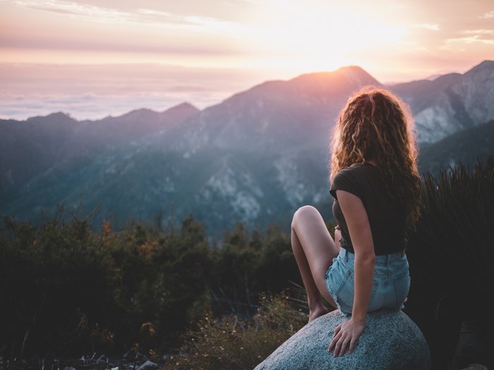Woman sitting on rock overlooking mountains at sunset
