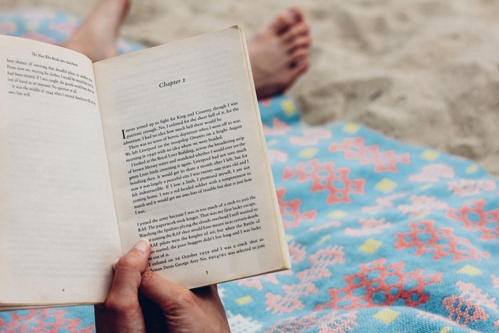 Person reading a book on a beach blanket