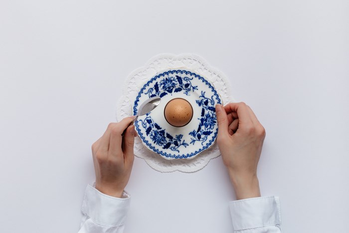 Person holding a boiled egg on a plate with a spoon