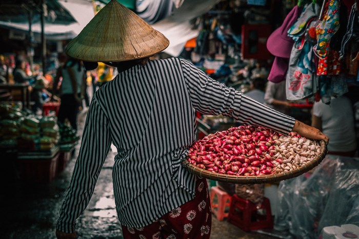 Person wearing a conical hat carrying produce at a market