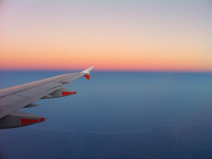Airplane wing over ocean at sunset