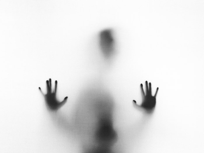 Silhouette of a person with hands pressed against frosted glass