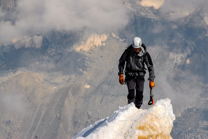 Man climbing a snowy mountain peak with ice axe