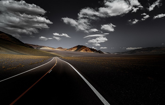 Road through a desolate landscape with mountains and clouds