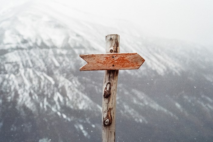 Wooden signpost pointing right in front of a snowy mountain