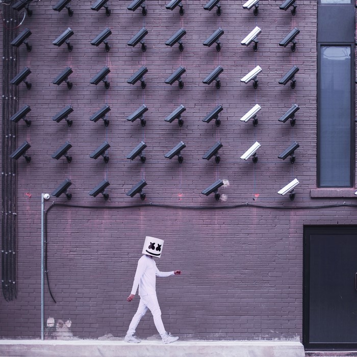 Marshmello walks past a wall of security cameras
