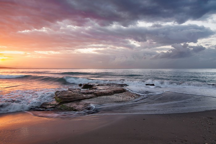 Beach with waves and rocks at sunrise in Malaga
