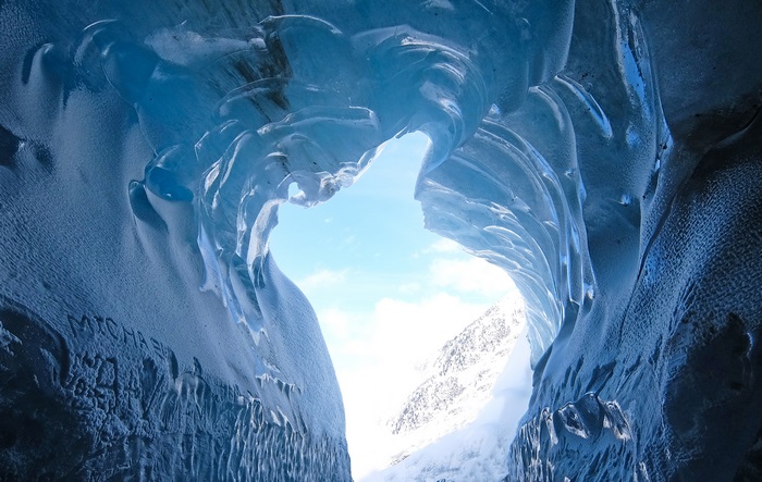 Inside a blue ice cave with sky and mountains visible
