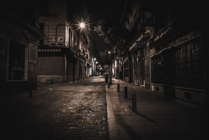 Dark alleyway at night with streetlights and cobblestone pavement