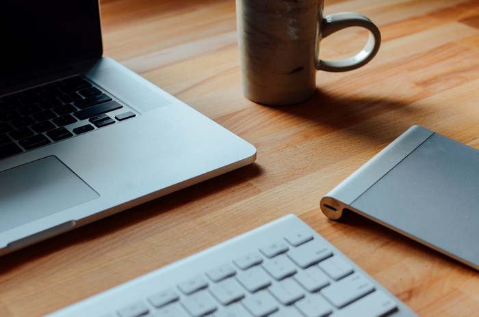MacBook, keyboard, mug, and tablet on a wooden desk