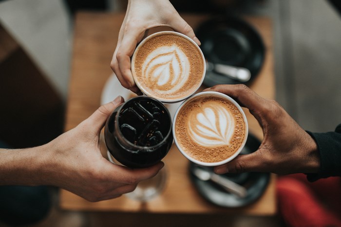 Three hands holding coffee and cold brew