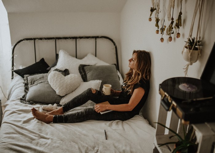 Woman with coffee and notebook on bed with record player