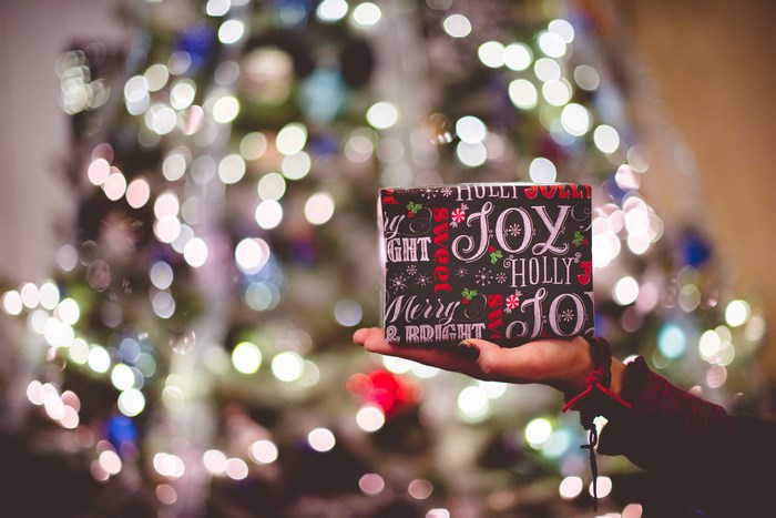 Hand holding a Christmas gift in front of a bokeh tree