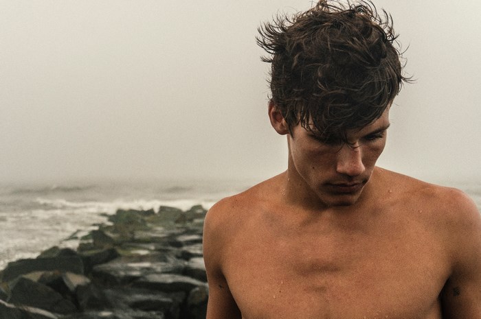 Shirtless man on rocky coast in fog