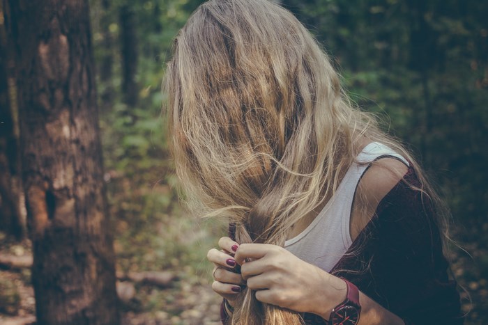 Woman braiding blonde hair in a forest