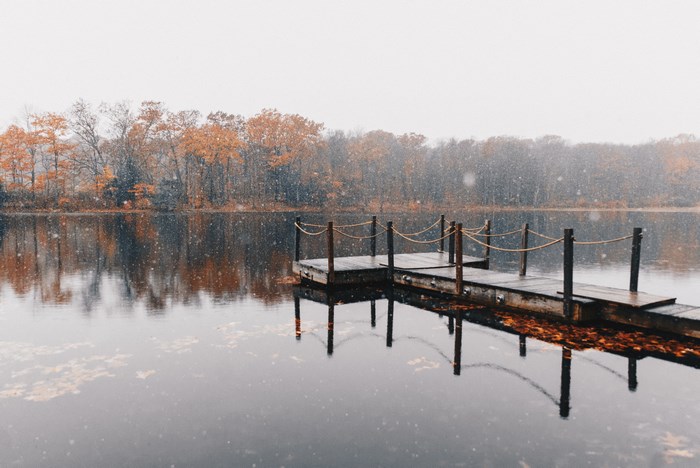 Wooden dock on a lake with autumn trees and snow