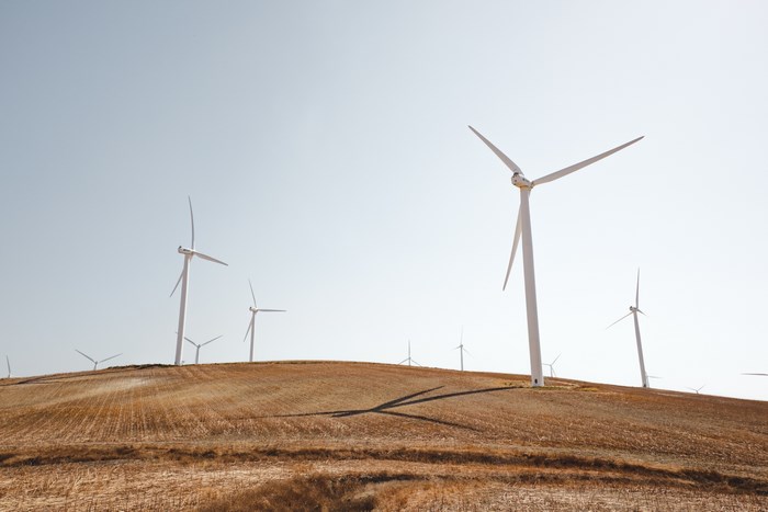 Wind turbines on a dry, rolling hill under a clear sky