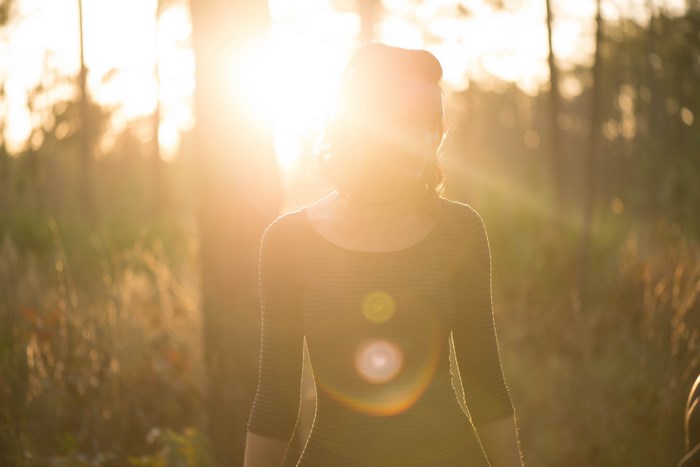 Woman Standing in Forest with Sun Flare