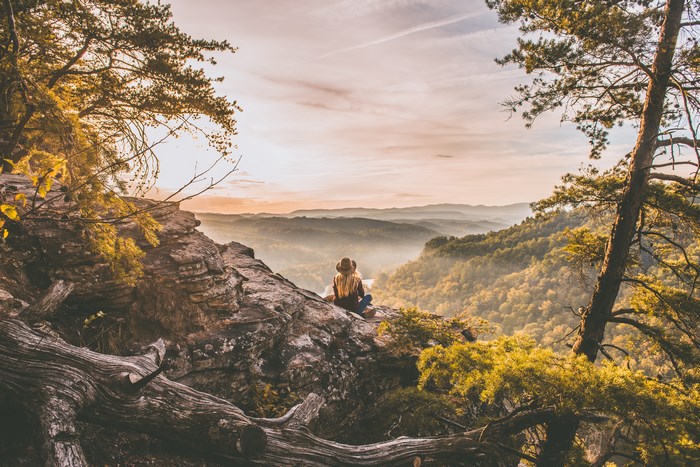 Woman sitting on a rock overlooking a misty mountain valley at sunrise