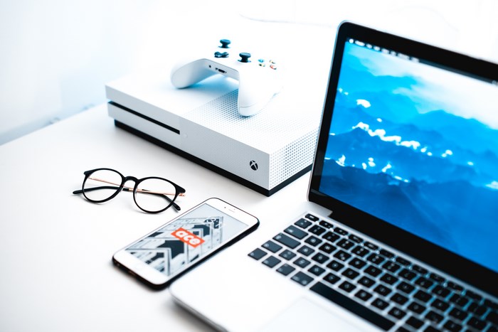 White Xbox console with controller, laptop, phone, and glasses