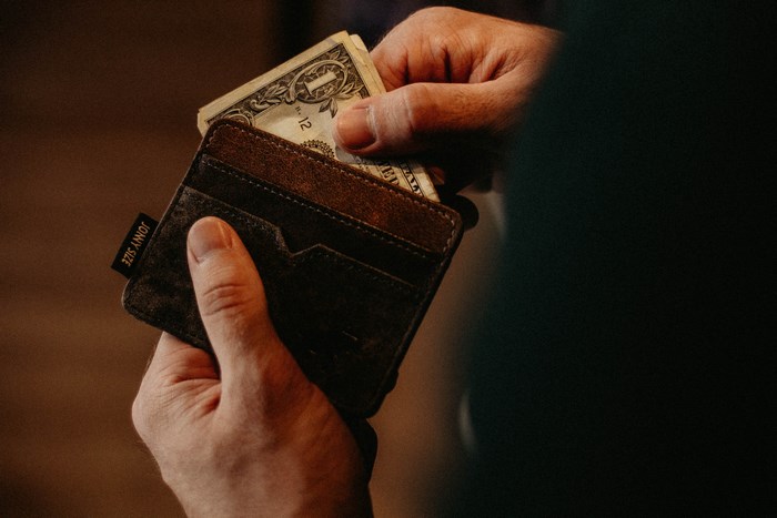 Person holding a brown leather wallet with US dollars