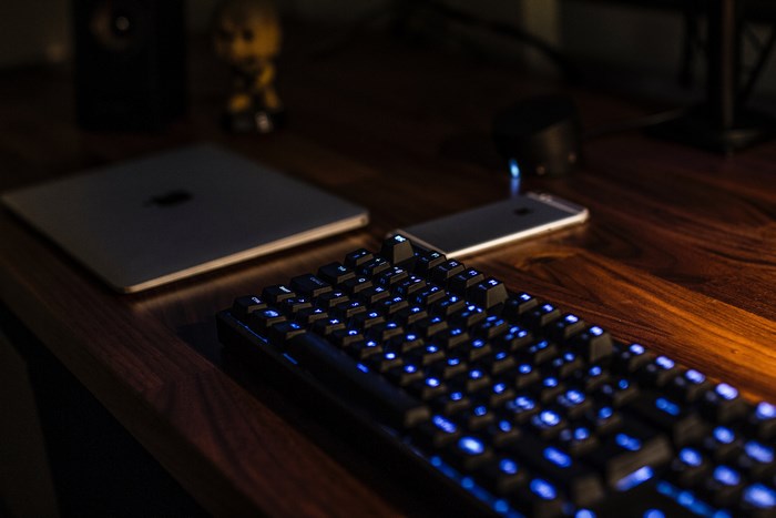 MacBook, iPhone, and illuminated keyboard on a wooden desk
