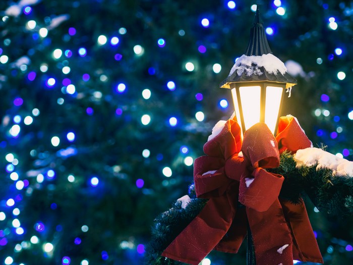 Snow-covered lantern with red bow and bokeh lights