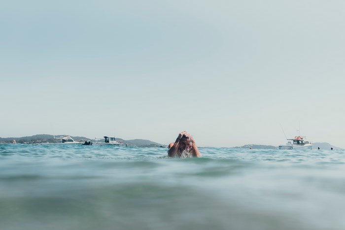 Person swimming in the ocean with boats in the background