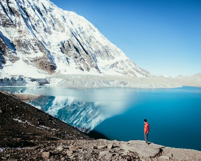Man standing by a blue lake with snow-capped mountains