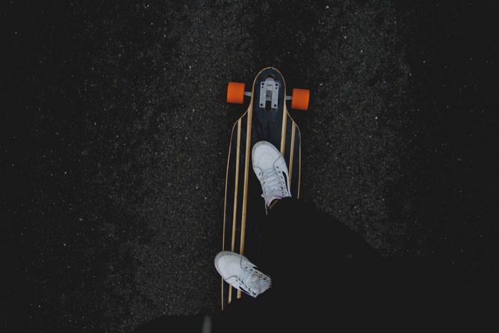 Skateboarder's feet on a longboard with orange wheels