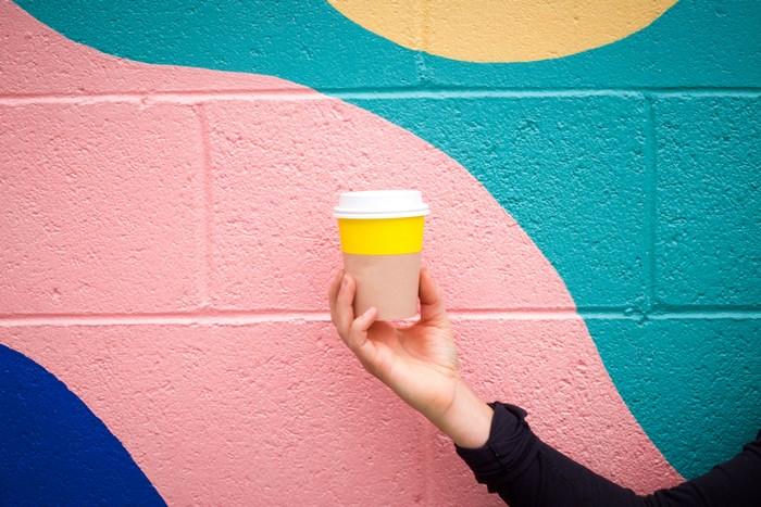 Hand holding a coffee cup against a colorful painted wall