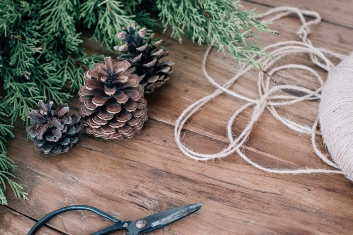 Pine cones, greenery, twine, and scissors on a wooden table