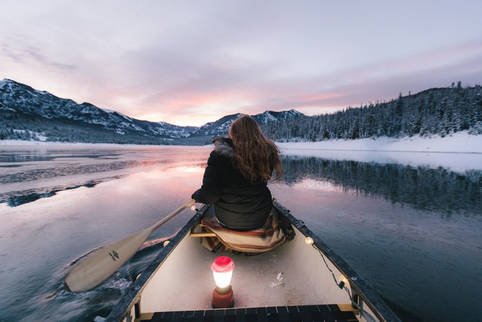Woman in canoe on frozen lake at sunset