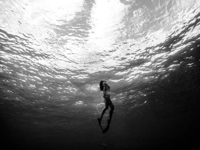 Woman free diving underwater with sun rays