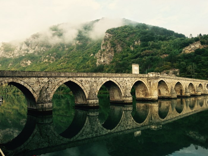 Stone bridge with arches over a river with mountain backdrop