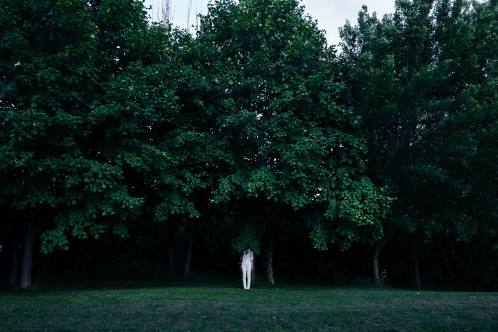 Person in white stands in a dark forest