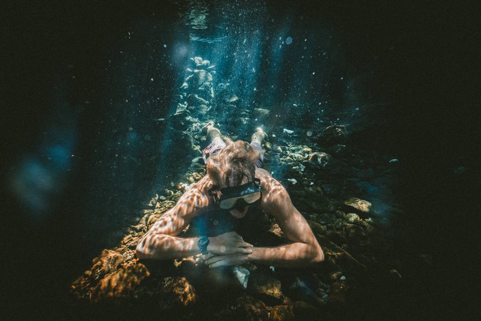 Underwater diver resting on rocks with sunbeams