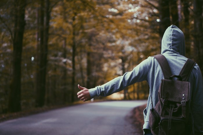 Person with backpack hitchhiking on a forest road