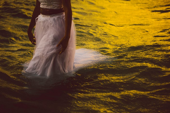Woman in wedding dress walking in golden water