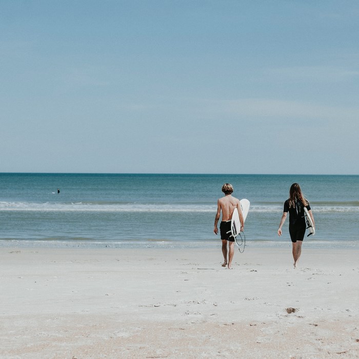 Man and woman carrying surfboards on a beach