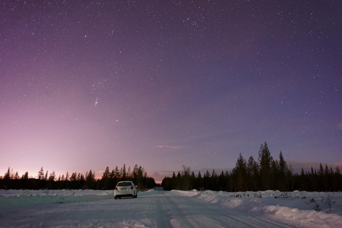 Car on snowy road under starry Lapland night sky